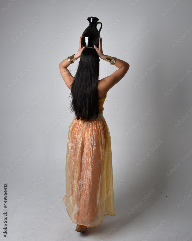 Wall mural full length portrait of pretty young asian woman wearing golden arabian robes like a genie, standing