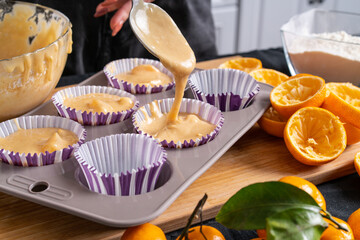 Woman pours batter from spoon into silicone mold for baking orange and tangerine muffins. Preparing for festive home meal.