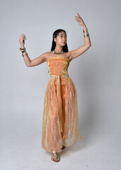 Full length portrait of pretty young asian woman wearing golden Arabian robes like a genie,...