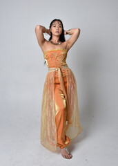 Full length portrait of pretty young asian woman wearing golden Arabian robes like a genie,...