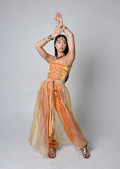 Full length portrait of pretty young asian woman wearing golden Arabian robes like a genie,...