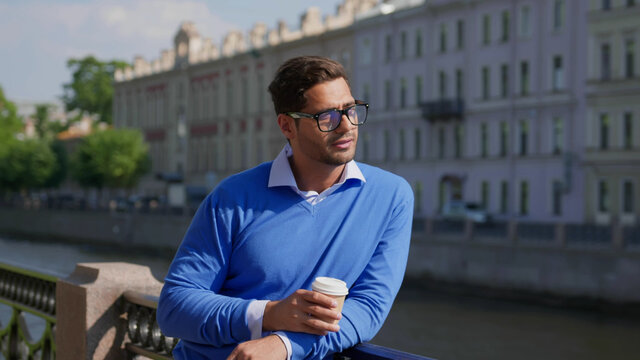 Young indian man smiling happy drinking coffee at city leaning on embankment railing