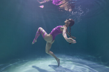 beautiful girl in a lilac swimsuit dancing underwater in the pool on a blue background