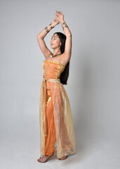 Full length portrait of pretty young asian woman wearing golden Arabian robes like a genie,...