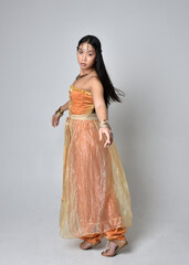 Full length portrait of pretty young asian woman wearing golden Arabian robes like a genie,...