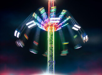 Blurry long exposure image of brightly lit amusement park rides.