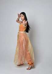Full length portrait of pretty young asian woman wearing golden Arabian robes like a genie,...