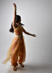 Full length portrait of pretty young asian woman wearing golden Arabian robes like a genie,...