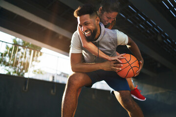 Man and woman friends playing basketball outdoors in city, having fun.