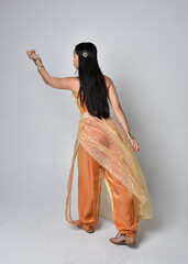 Full length portrait of pretty young asian woman wearing golden Arabian robes like a genie,...