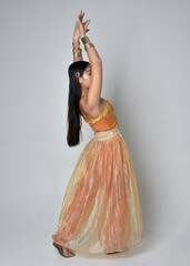 Full length portrait of pretty young asian woman wearing golden Arabian robes like a genie,...