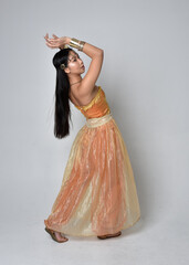 Full length portrait of pretty young asian woman wearing golden Arabian robes like a genie,...