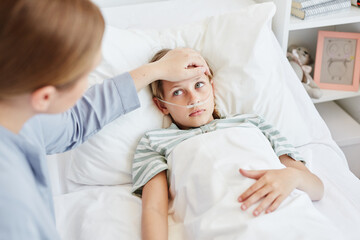 Portrait of caring mother by bed of sick child in hospital room, focus on little girl with oxygen support system