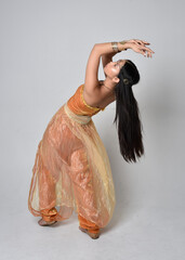 Full length portrait of pretty young asian woman wearing golden Arabian robes like a genie,...