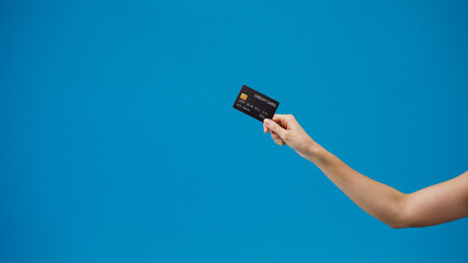 Young woman hand shows credit card for shopping online over blue background in studio. Copy space for place a text, message for advertisement. Advertising area, mockup promotional content.