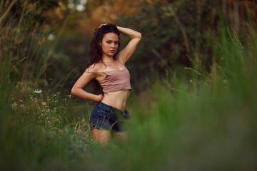 Naklejka na ściany i meble Beauty in nature woman enjoying the summer sun outdoors in the park or garden. Dressed jeans shorts and beige top in golden hour