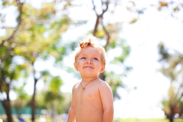 Smiling staying baby. The child is 1 year old. Sunny kid portrait . close up.portrait of pretty babe boy looking at copy space.photo on blurred background.Smiling child in forest near beach.