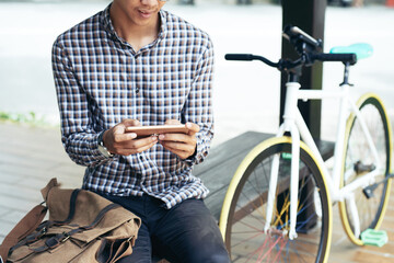 College student with textile bag sitting on bench and texting friends or checking mobile application