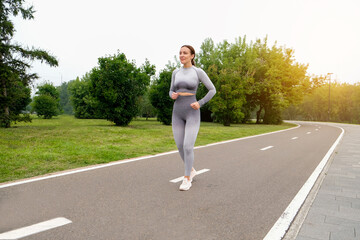 Woman dressed leggings and top running asphalt road summer park. Healthy lifestyle concept. Active and athletic female exercises