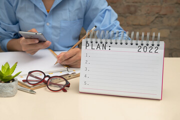 Woman using smartphone and writing down information for planning 2022.Closeup of blank notebook