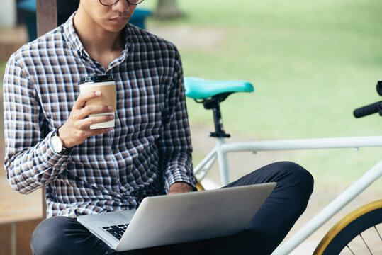 Cropped image of serious software developer sitting on bench in park, drinking coffee and working on new big project