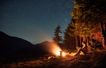 Side view of silhouette of woman having a rest near forest in campsite. Female is sitting near...
