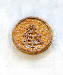 Delicious homemade festive New Year's biscuit cream cake, decorated with a christmas tree made of cream and sugar snowflakes made of glaze on a textured white background