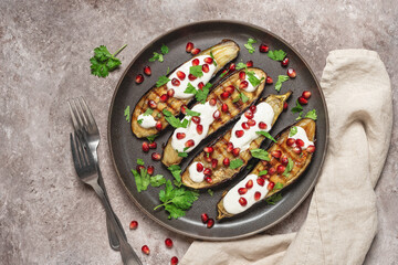 Grilled eggplants with yogurt sauce and pomegranate on a brown grunge background. Top view, flat lay