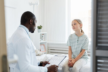 Obraz premium Portrait of teenage girl talking to doctor while sitting on bed in hospital room