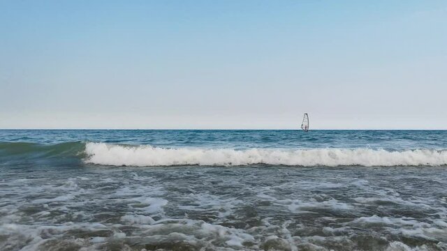 Sailboat sails on the waves. Small waves breaking on the shore. Shot 4K on the beach the Black Sea.
