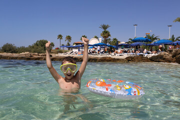 Swiming happy boy, child with life-saving inflatable circle in Ayia Napa, Cyprus. Nissi Beach. Summer swim. Bathing kid in water. Active sea recreation. Summer swim, travel. Bathing child in water