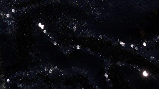 Black shiny background. Bright highlights shine and glow on black fabric.
