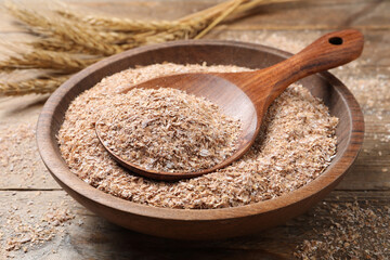 Wheat bran and spoon in bowl on wooden table