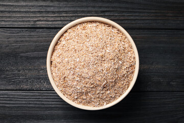 Bowl of wheat bran on black wooden table, top view