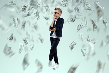 A cute, rich boy with glasses holds dollars and knows how to make money against the background of...