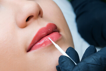 permanent makeup on her lips at the beautician salon. Applying liquid glass to lips