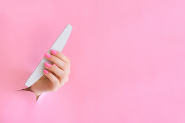 nail file in the hand of a young woman on a pink background from the hole.