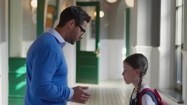 Side view of indian male teacher reprimanding preteen schoolgirl in corridor