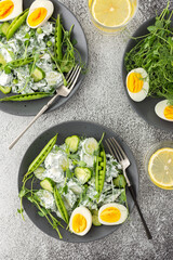 Obraz na płótnie Canvas Salad with arugula, cucumbers and young peas with yogurt and boiled eggs with microgreens, lemon water in a glass, top view