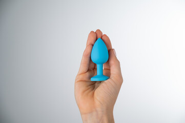 Woman holding a blue butt plug on a white background. Adult toy for alternative sex