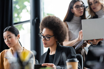 young african american businesswoman in eyeglasses working in office near blurred colleagues