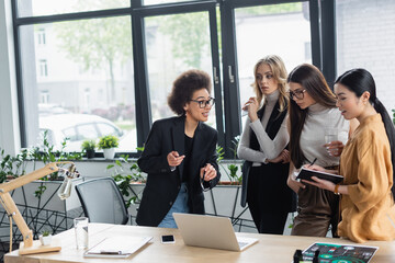 african american woman pointing at laptop while talking to multiethnic business partners