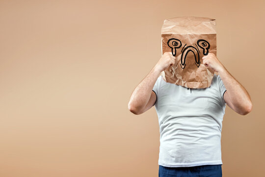 Men put a paper bag on their heads, on which a crying face, upset, bad mood is drawn. Isolated on yellow background, images are easy to crop for use anywhere, copy space.