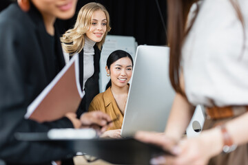 interracial businesswomen working near computer monitor and colleagues on blurred foreground