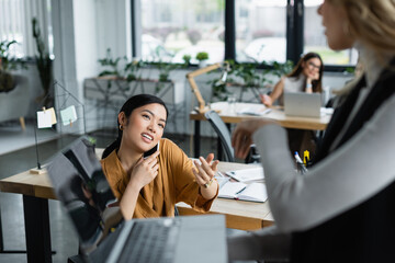 asian businesswoman talking to blurred colleague while calling on mobile phone