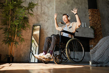 Full length portrait of modern disabled man in wheelchair enjoying music at home, copy space