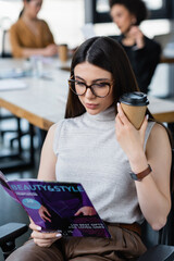 brunette businesswoman with coffee to go reading beauty and style magazine