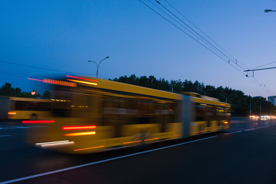 The movement of a blurred bus along the avenue in the evening.