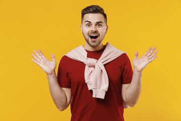 Amazed surprised impressed fun happy young man 20s wear red t-shirt casual clothes spread hands look camera isolated on plain yellow color wall background studio portrait. People lifestyle concept