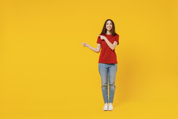 Full size body length young brunette woman 20s wear basic red t-shirt point aside on workspace area copy space mock up isolated on yellow background studio portrait. People emotions lifestyle concept